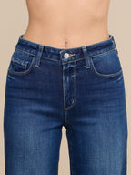 Close-up of a person wearing dark blue denim jeans, showing the waist, hips, and front pockets against a plain beige studio background.