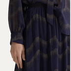 A close-up of a navy blue long-sleeve dress with a textured, wavy metallic pattern in a champagne-gold tone, featuring a matching waist tie belt.
