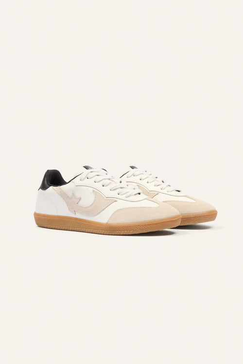 Pair of white sneakers with brown soles on a light beige background