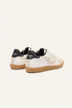 White sneakers with black soles and brown soles on a light gray background