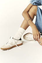 Person wearing white sneakers and white socks on a light background