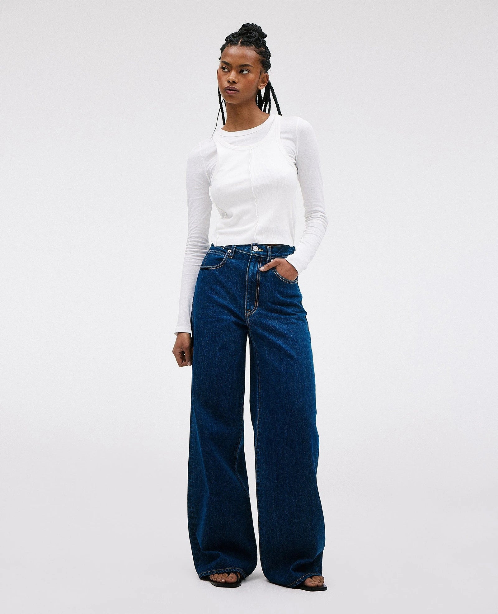 A person standing wearing high-waisted, wide-leg jeans and a white long-sleeve top.