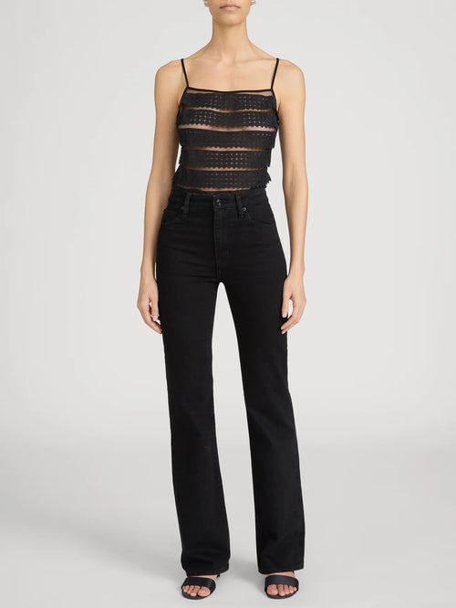 Person wearing a black lace top and black pants on a white background frame the arrow