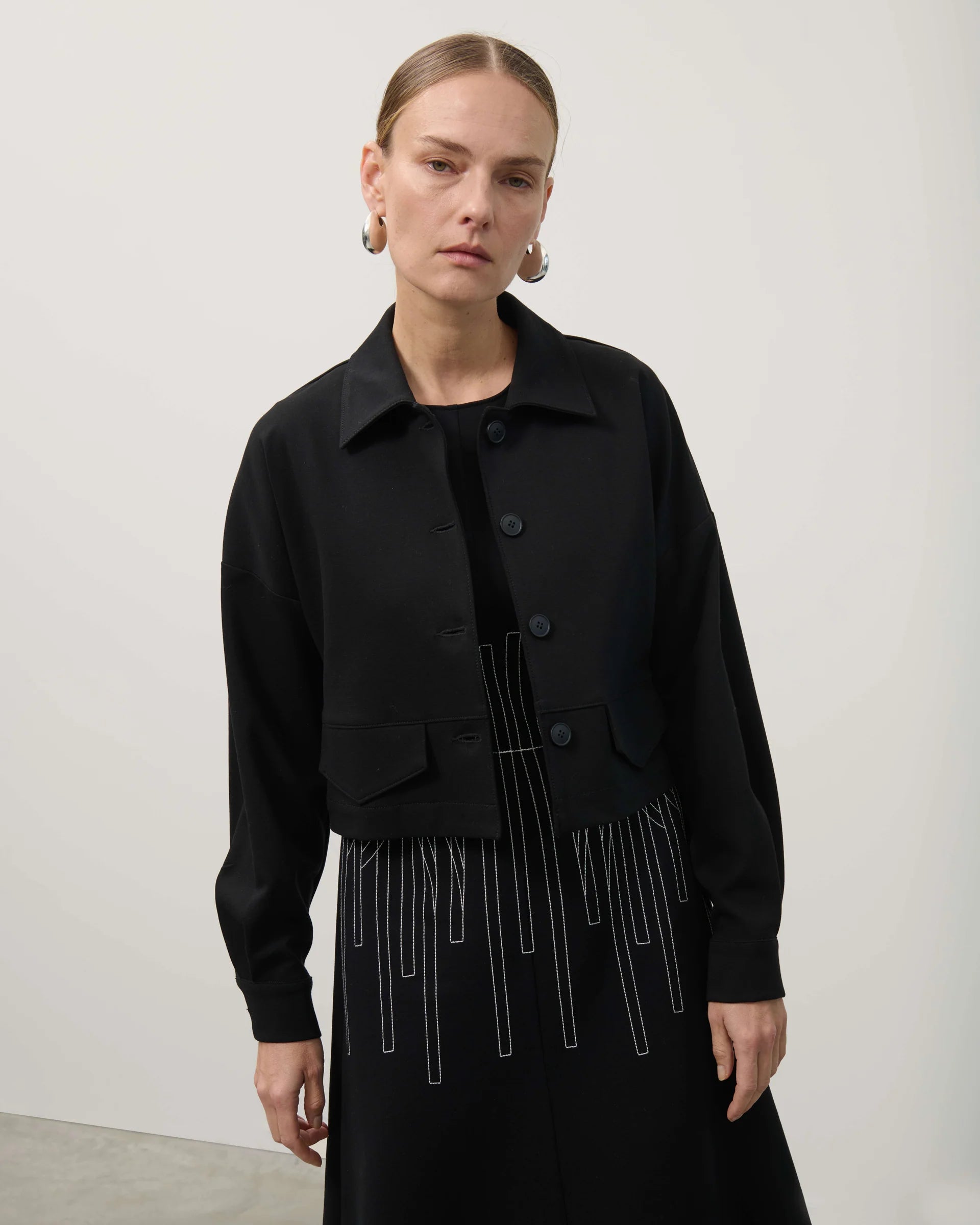 Person wearing a black jacket with fringe details on a plain background