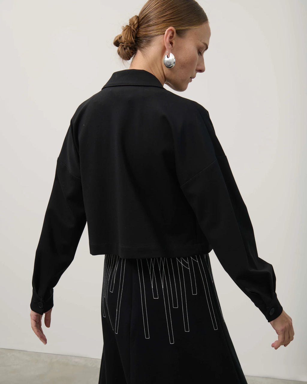 Woman wearing a black outfit with long sleeves and a high collar against a white background