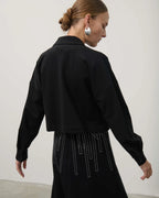 Woman wearing a black outfit with long sleeves and a high collar against a white background