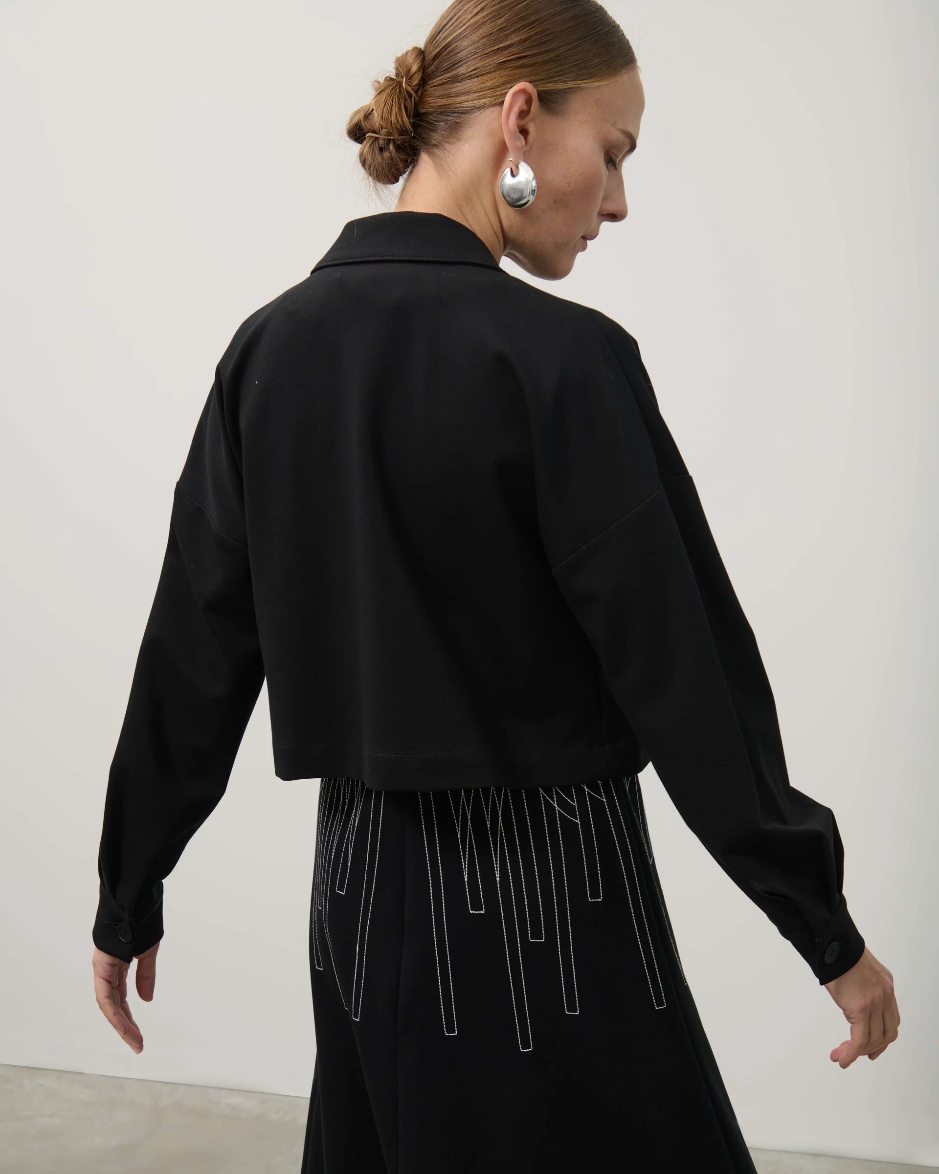 Woman wearing a black outfit with long sleeves and a high collar against a white background