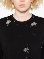 Black sweater with dragonfly embellishments worn by a person with blonde hair.