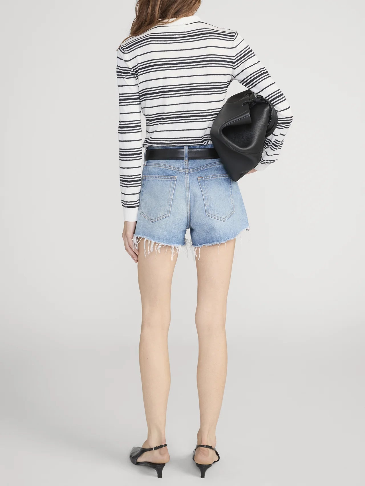 Person wearing a striped sweater and denim shorts on a plain background