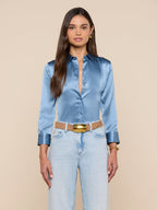 Woman wearing a light blue satin shirt and jeans with a beige background