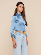 Woman wearing a light blue satin shirt and light blue jeans against a beige background