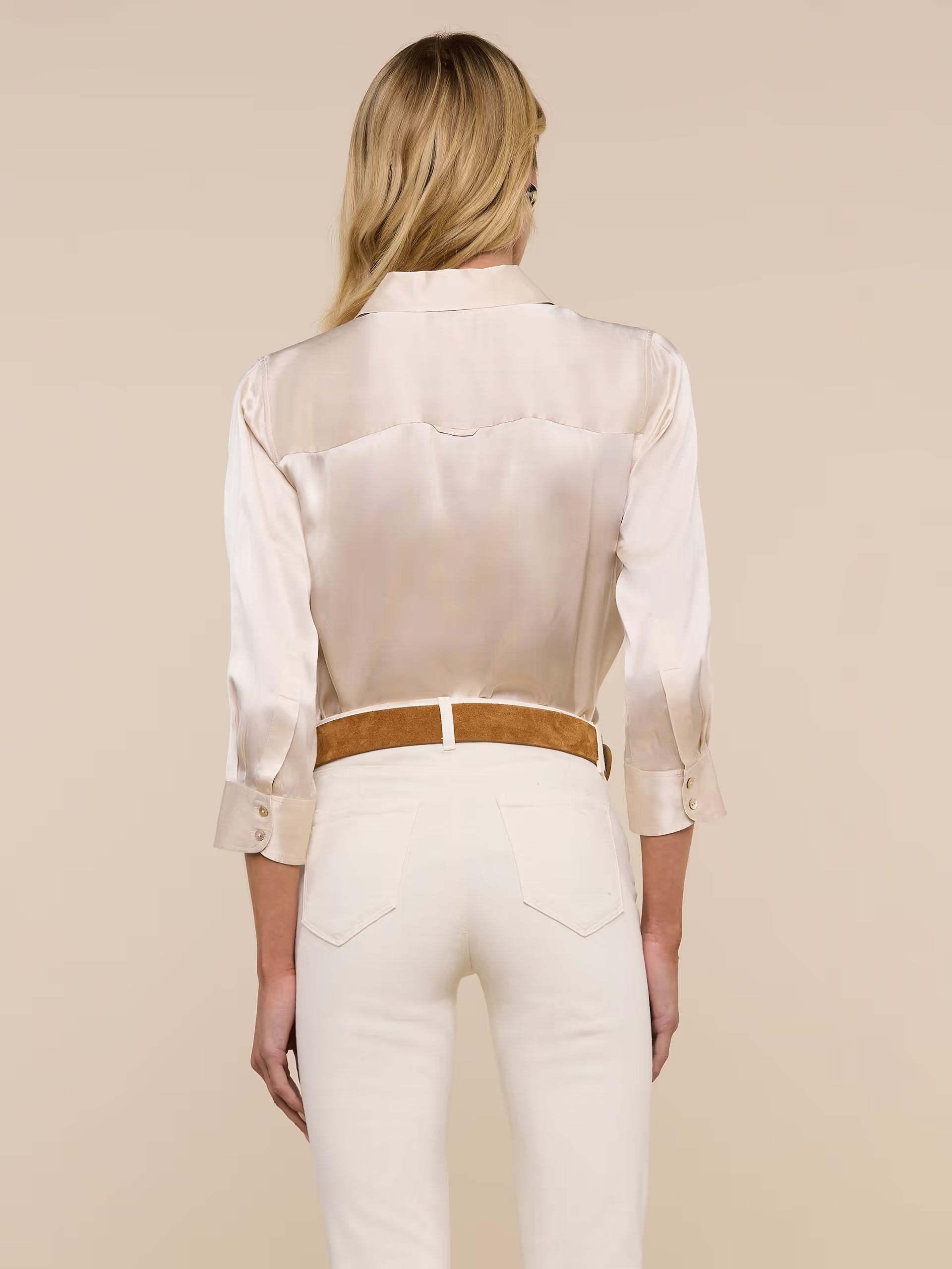 Woman wearing a white blouse and white pants with a brown belt on a beige background