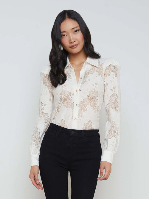 Woman wearing a white lace blouse and black pants against a plain background