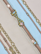 Close-up of a gold chain belt with pink buckles on a light blue background