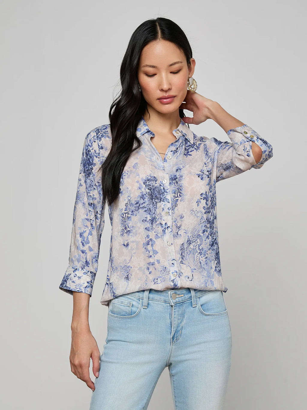 Woman wearing a floral blouse and light blue jeans against a gray background