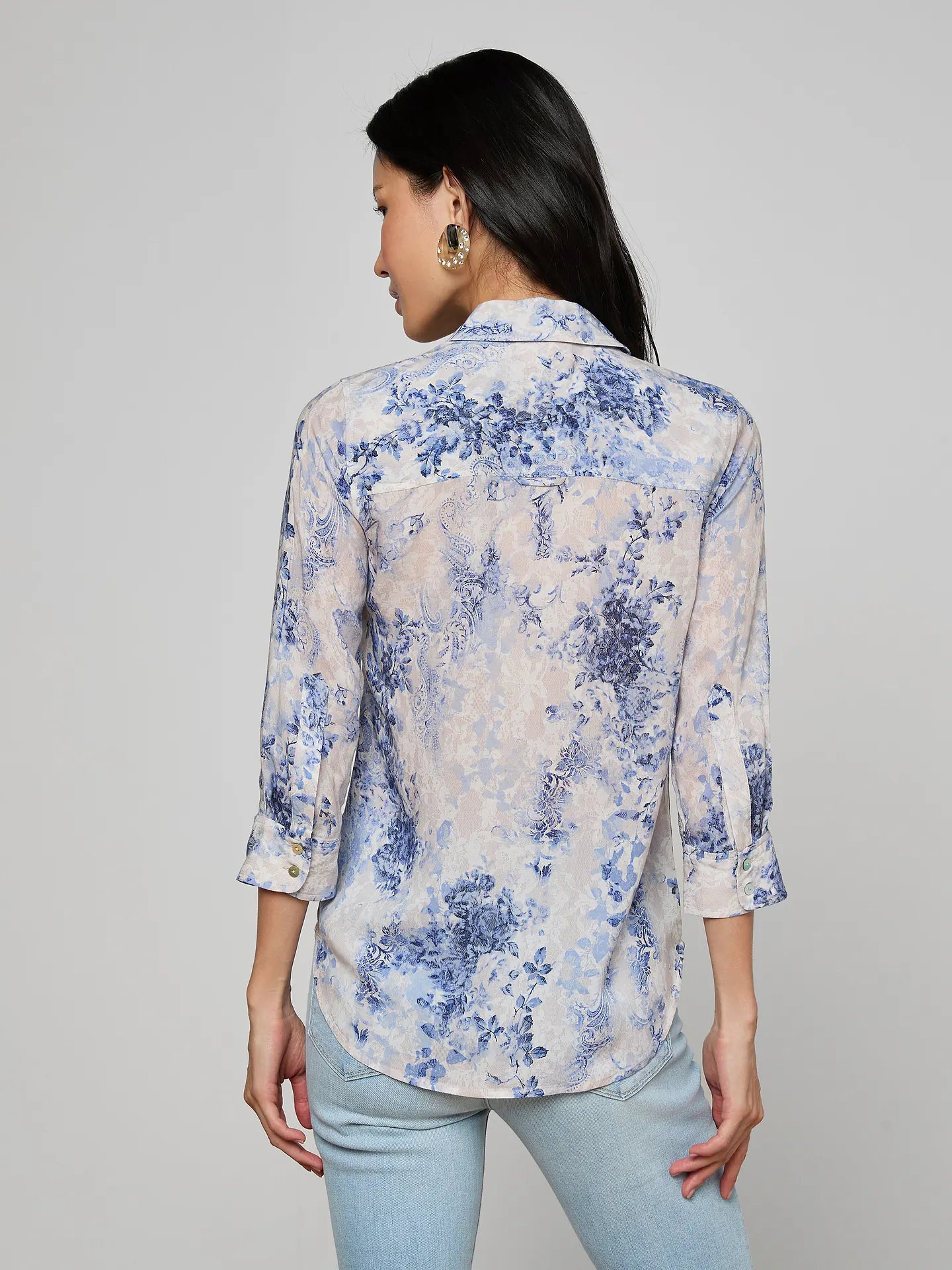 Woman wearing a floral blouse with rolled-up sleeves on a gray background
