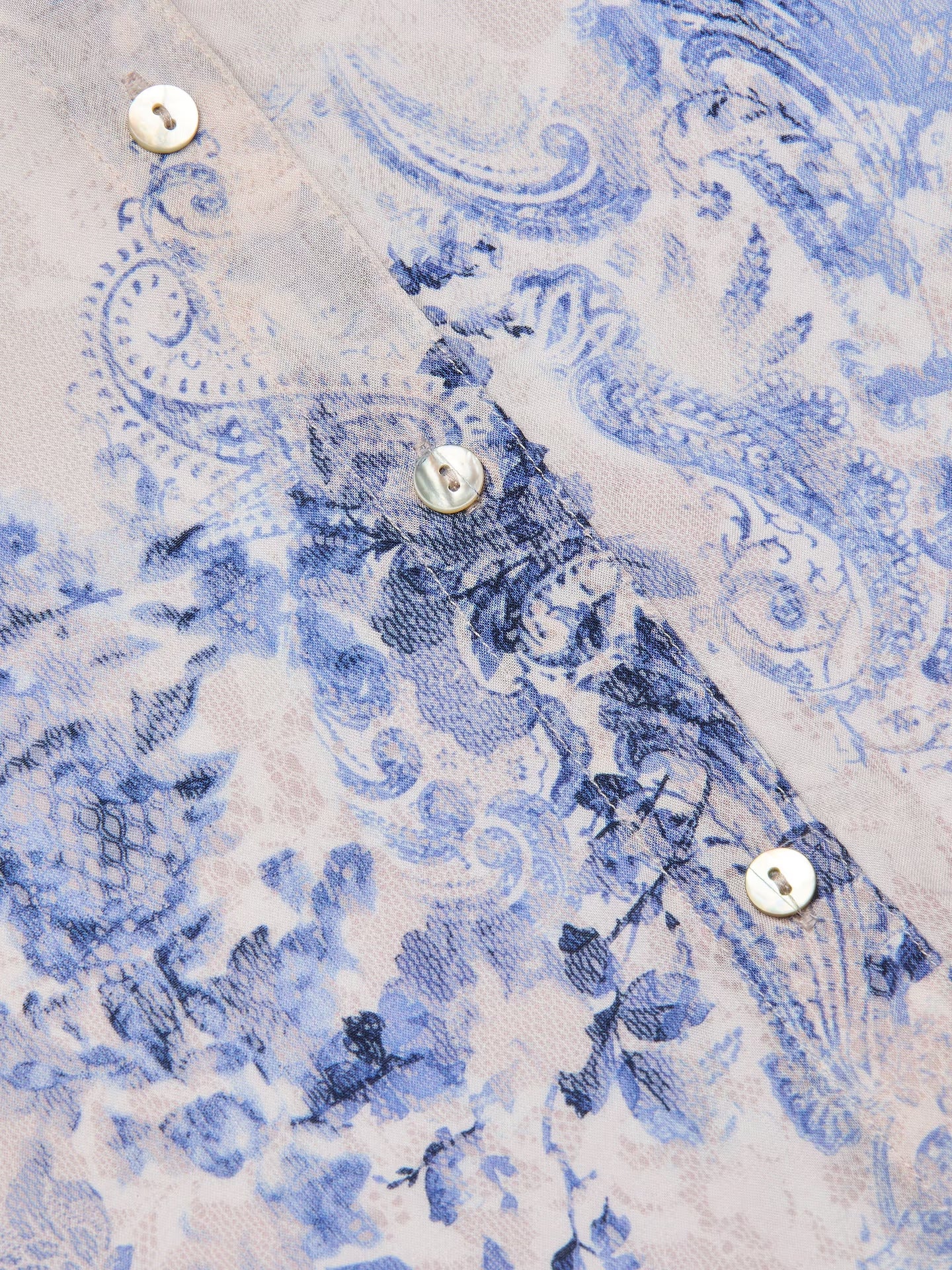 Close-up of a fabric with blue paisley pattern and metal buttons.