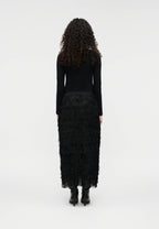 Person wearing a black top with a feathered like Sabrina skirt on a white background