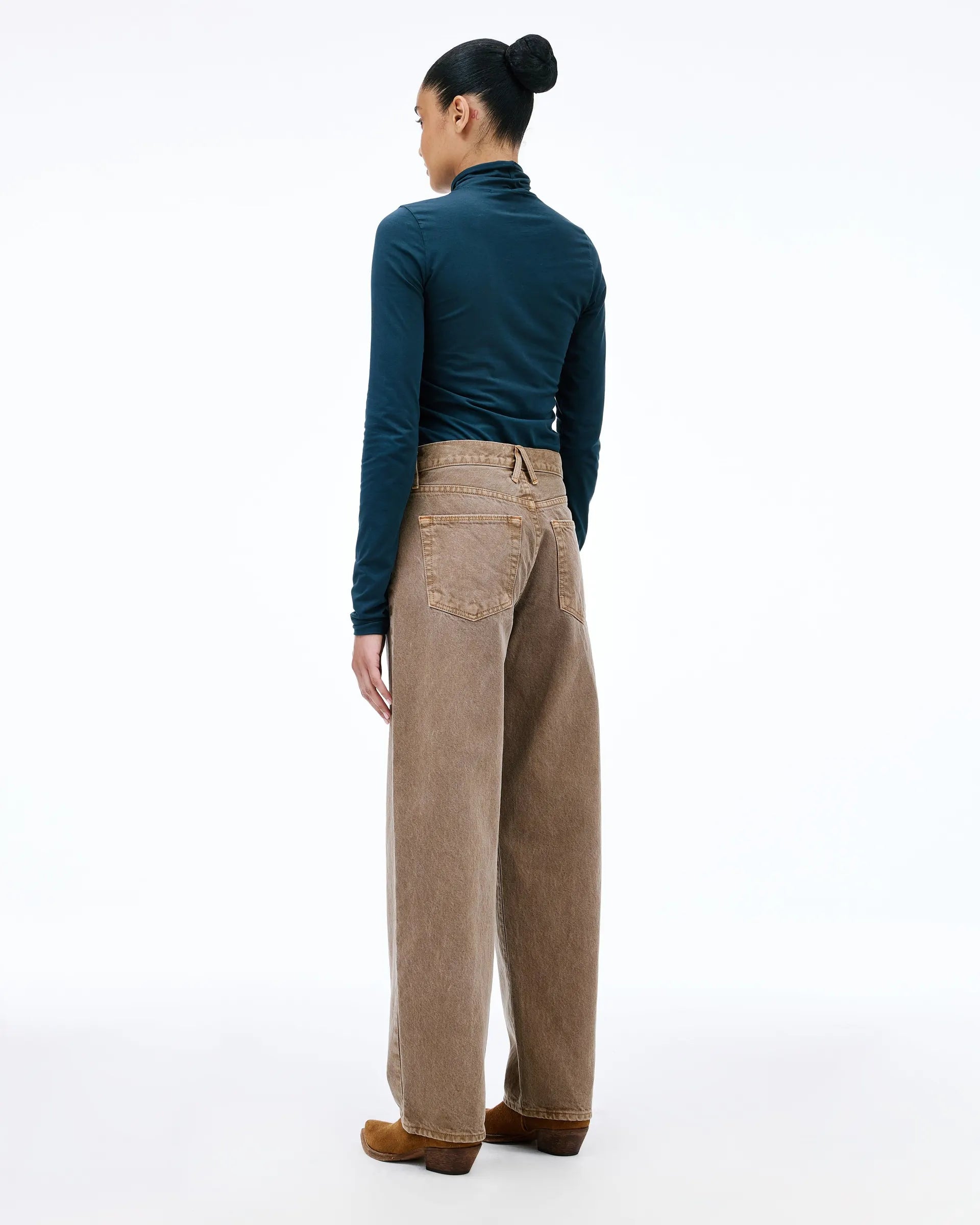 A model shown from the back wearing a dark teal long-sleeve mock neck top, beige wide-leg corduroy pants, and brown suede shoes, against a solid white studio background.