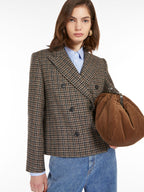 A woman wearing a houndstooth wool double-breasted blazer with a lapel collar and decorative buttons on sleeve cuffs paired with blue jeans.