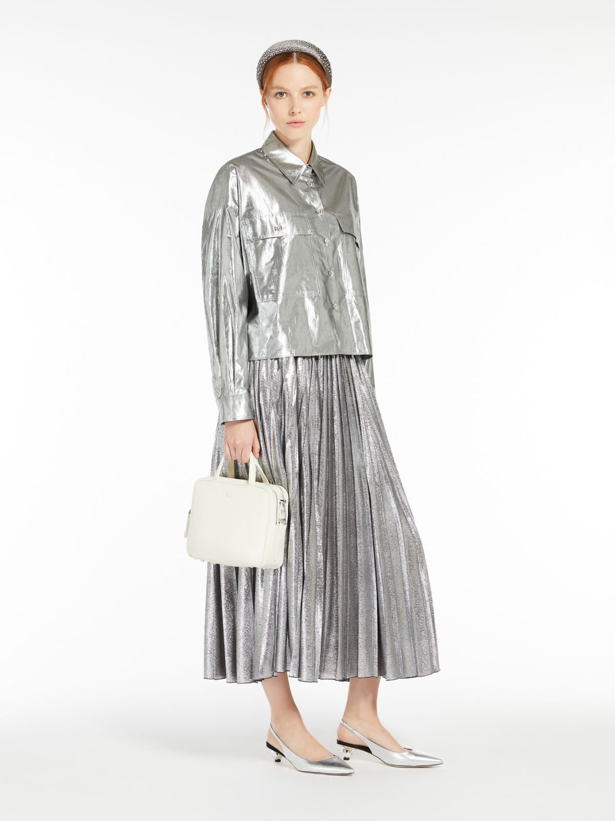 Woman wearing a silver metallic outfit with a white handbag on a white background