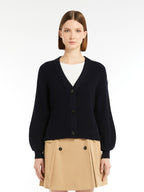 Woman wearing a navy cardigan over a white shirt and beige skirt on a white background