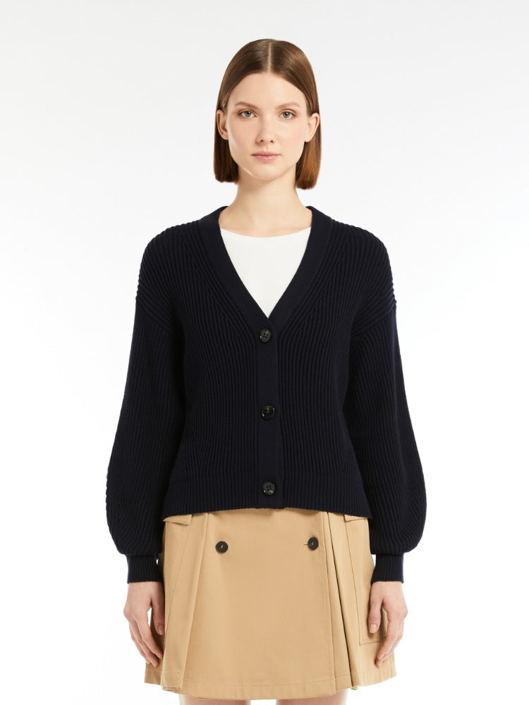 Woman wearing a navy cardigan over a white shirt and beige skirt on a white background