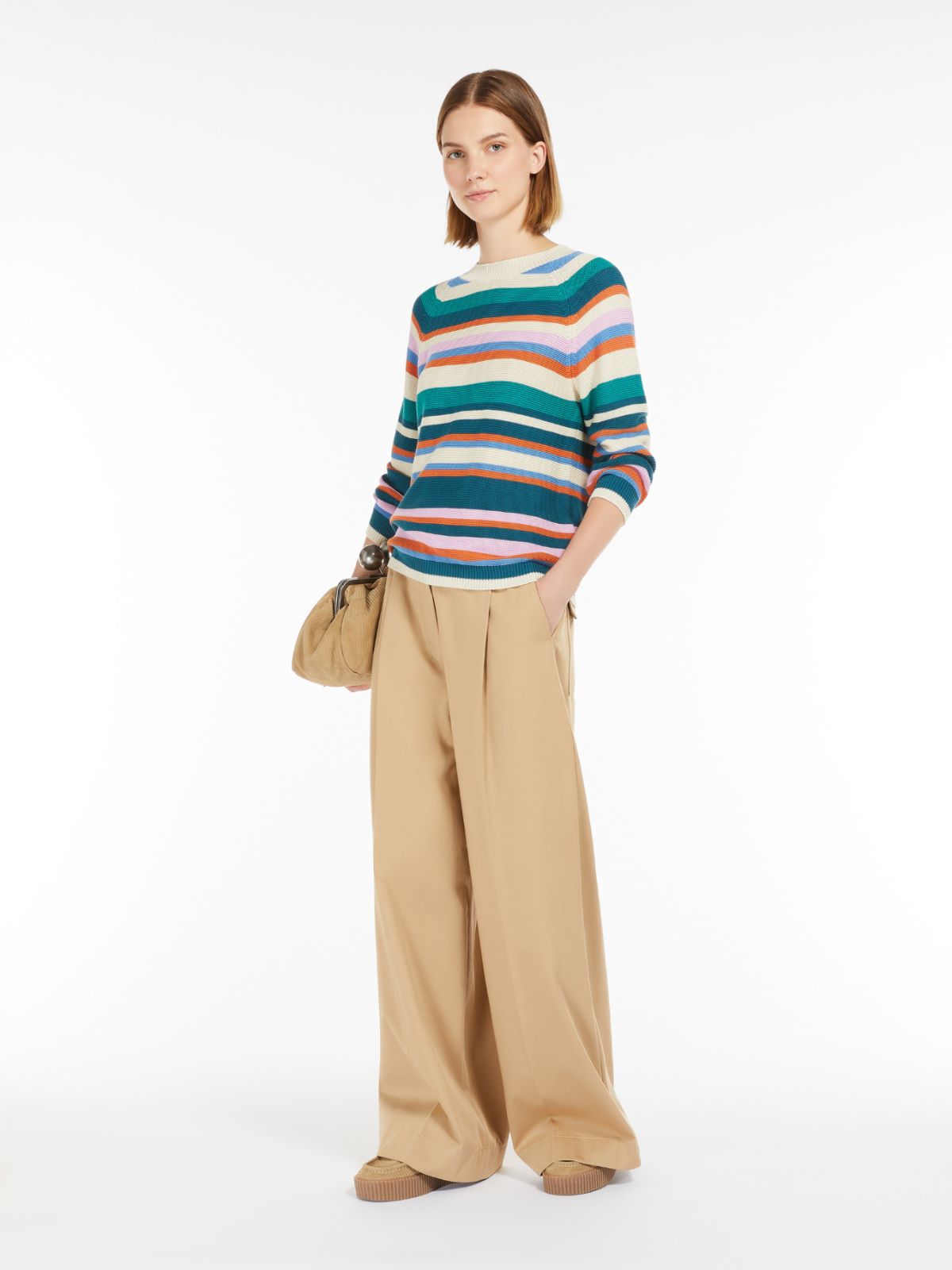 Woman wearing a colorful striped sweater and beige pants on a white background