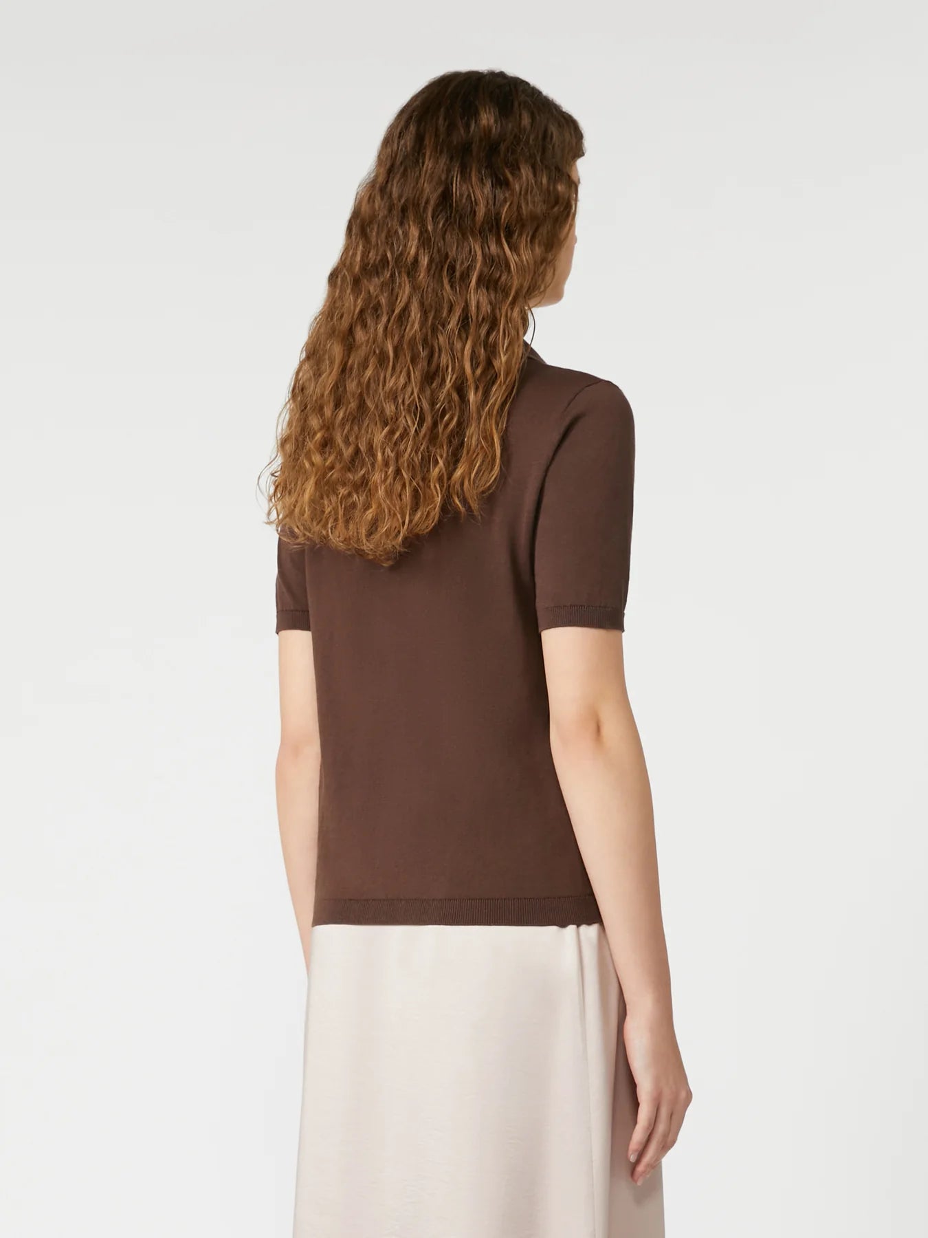 Woman wearing a brown top and white pants on a plain background