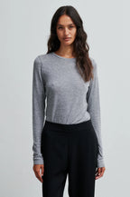 Woman wearing a gray long-sleeve top and black pants on a light gray background