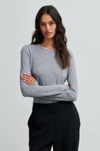 Woman wearing a gray sweater and black pants against a light gray background