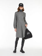 A model wearing a long sleeve, high neck, gray dress with an inverted pleat in the front, paired with black leggings and carrying a black bag with a logo on it.