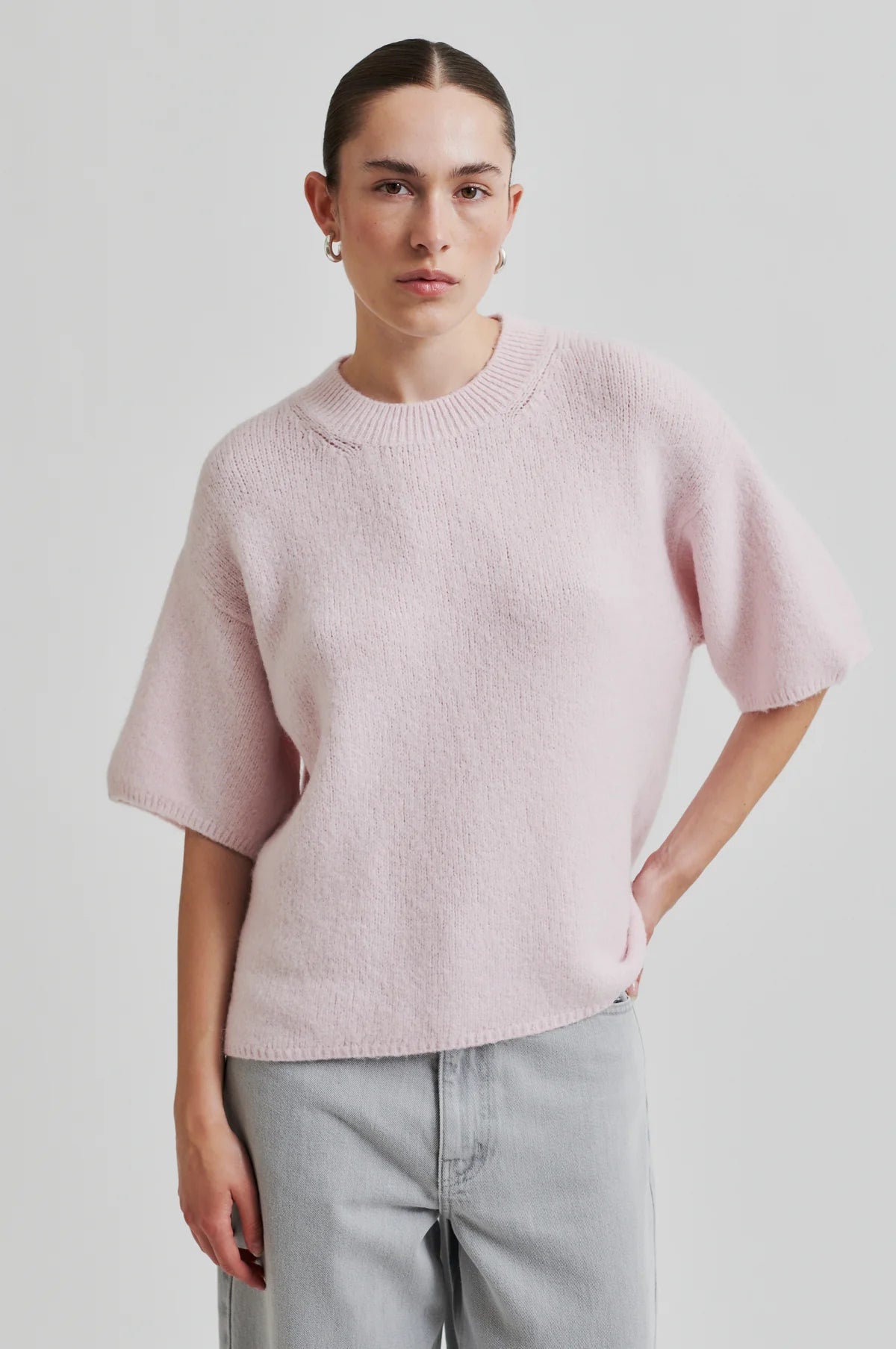 Person wearing a light pink sweater and light gray pants on a plain background