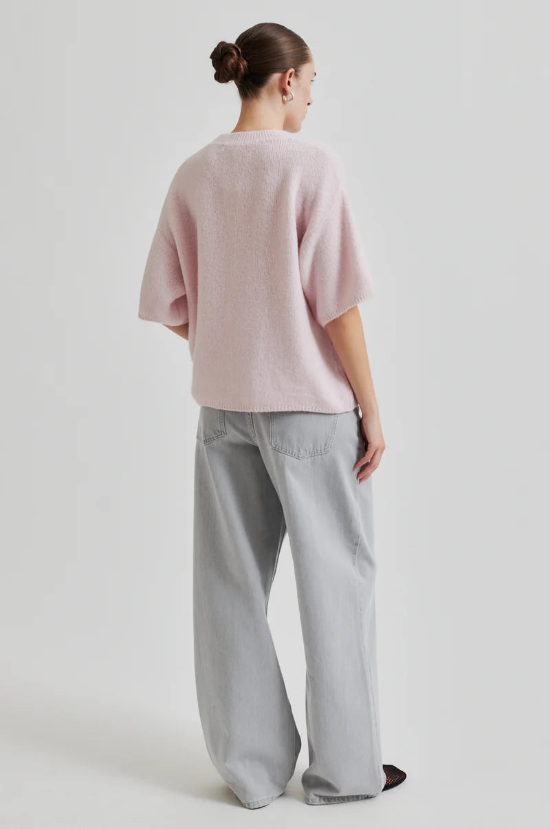 Person wearing a pink sweater and light gray pants on a white background