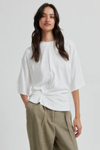 Woman wearing a white second female blouse and green pants on a plain background.shop online. 