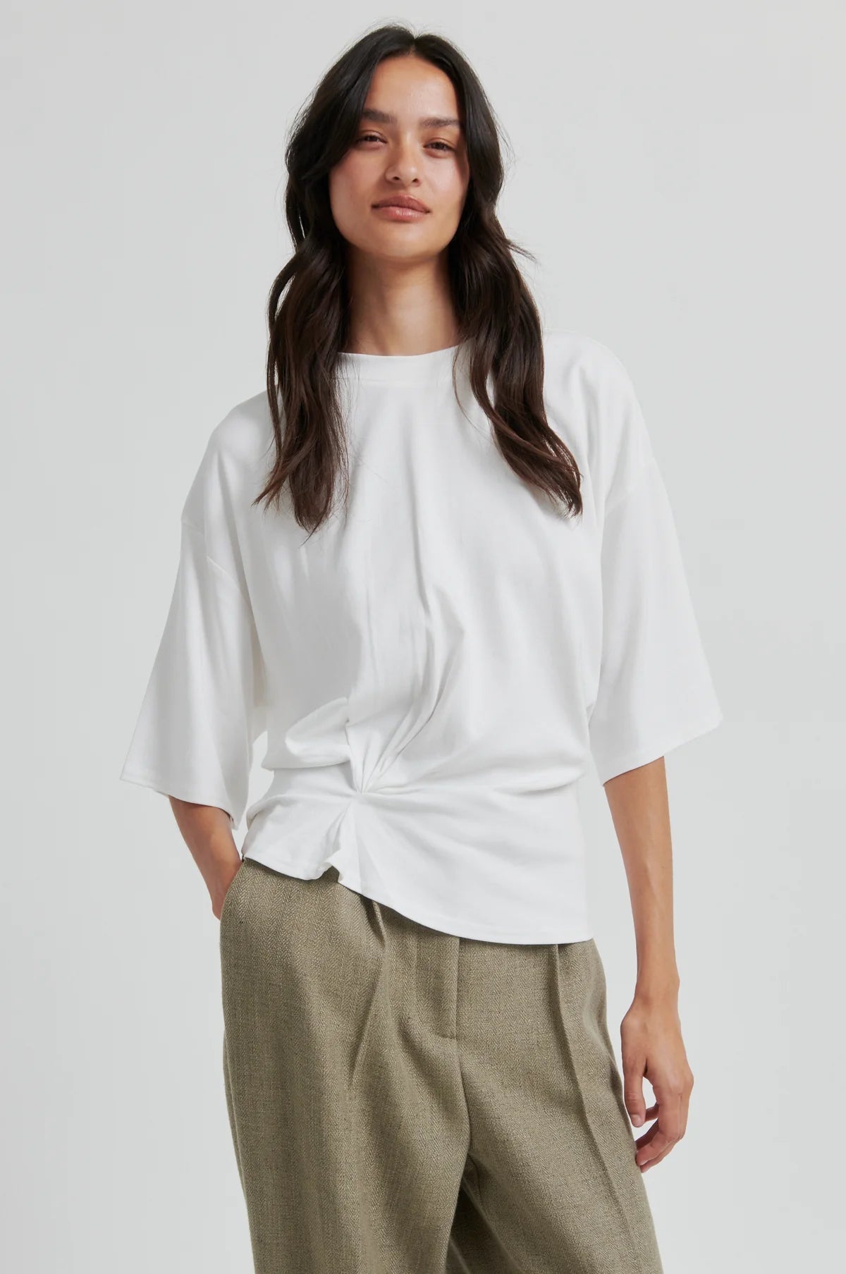 Woman wearing a white second female blouse and green pants on a plain background.shop online. 
