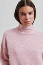 Person wearing a pink turtleneck sweater against a plain background