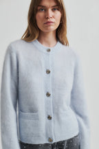Woman wearing a second female  light blue cardigan with buttons against a plain background.shop online 