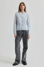 Woman wearing a light blue cardigan and dark patterned pants on a white background