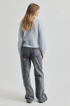 Person wearing a light gray sweater and dark gray jeans on a white background