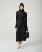 Woman wearing a black lace dress with sheer long-sleeve top against a white background