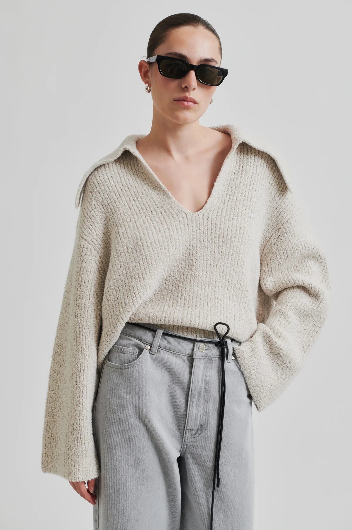 Person wearing a second female beige knitted sweater and light gray pants against a plain background