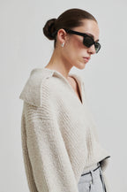 Woman wearing a textured beige cardigan and sunglasses on a plain background