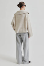 Person wearing a beige knitted sweater and light gray pants on a white background