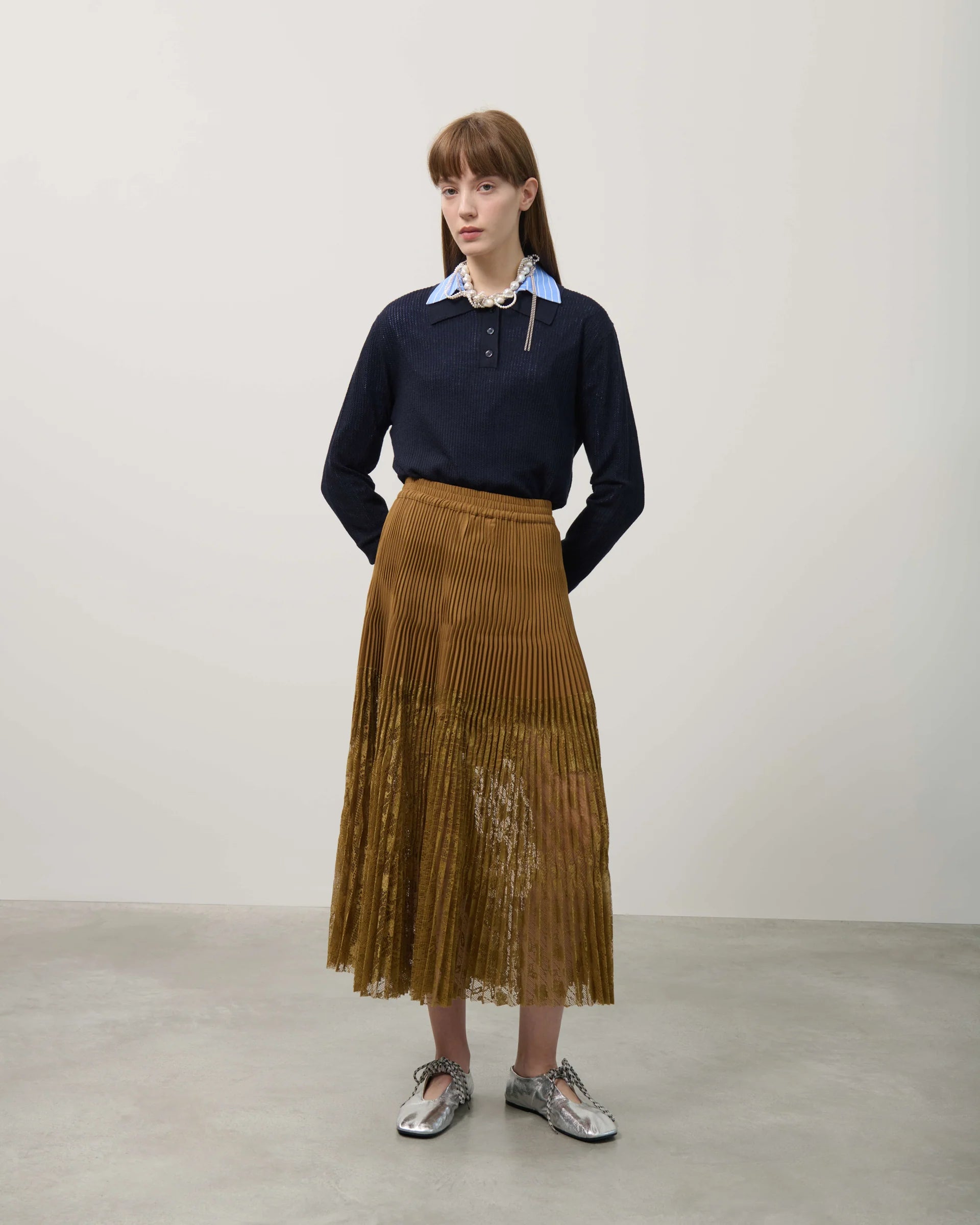 Woman wearing a navy sweater and brown pleated skirt against a plain background