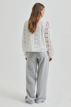 Person wearing a white lace top and gray pants on a plain background