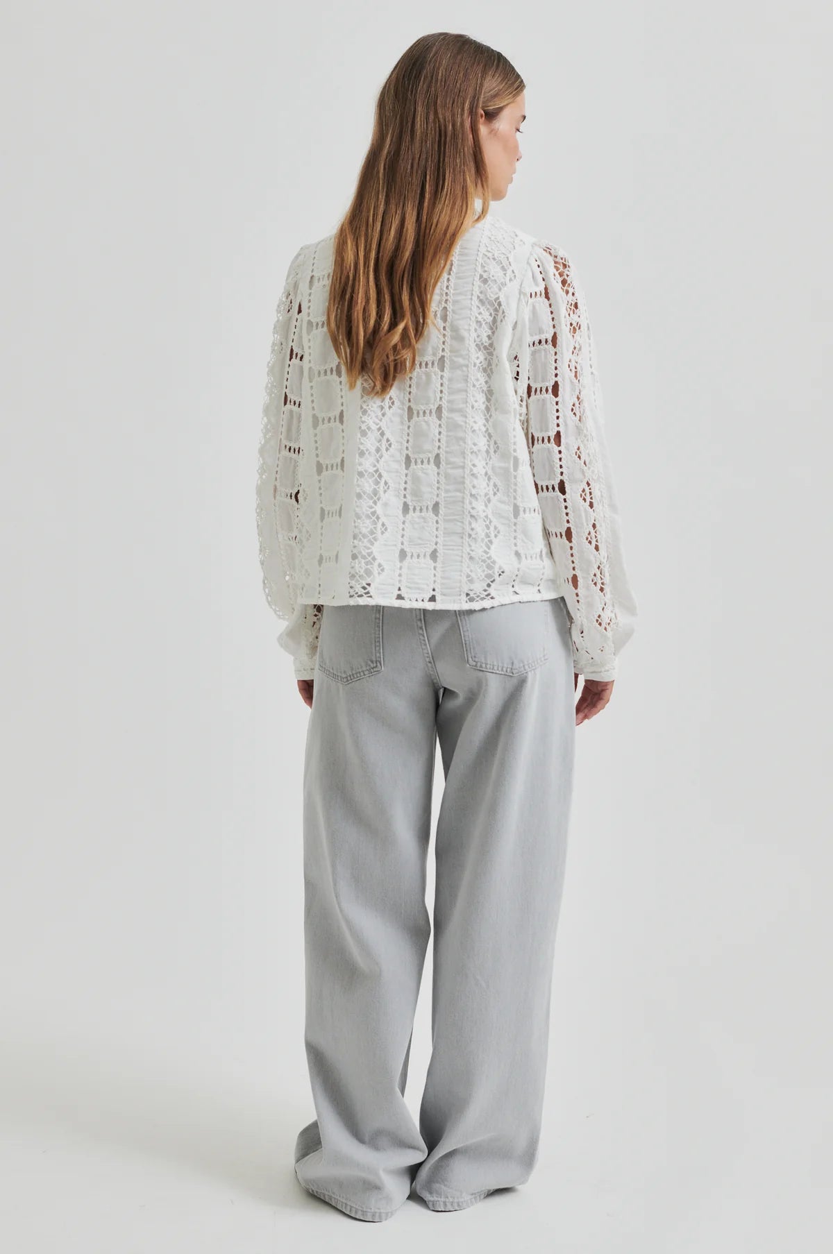 Person wearing a white lace top and gray pants on a plain background