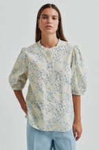 Woman wearing a second female floral blouse with puffed sleeves on a plain background.shop online.