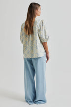 Woman wearing a floral blouse and light blue pants on a white background