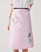 Pink skirt with floral embroidery worn by a person on a light gray background